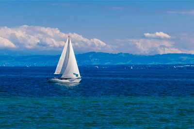 Velero navegando en agua azul con la montaña y las nubes de fondo
